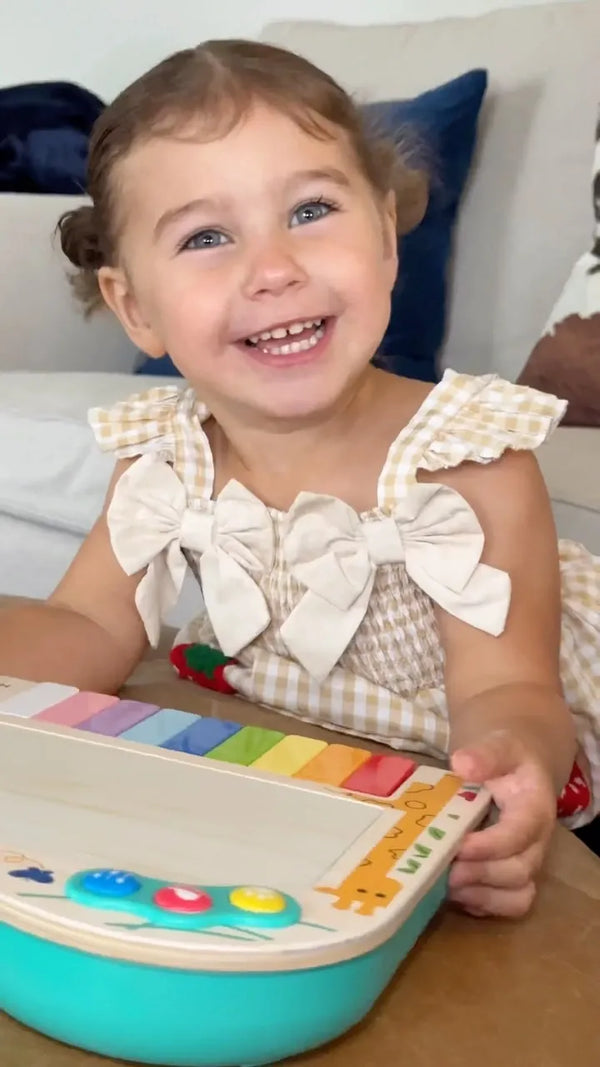 Menina sorrindo com o piano de pixels Hape no colo
