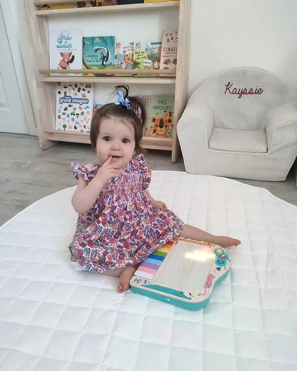 Bebê sentada no tapete com o piano de pixels Hape aceso