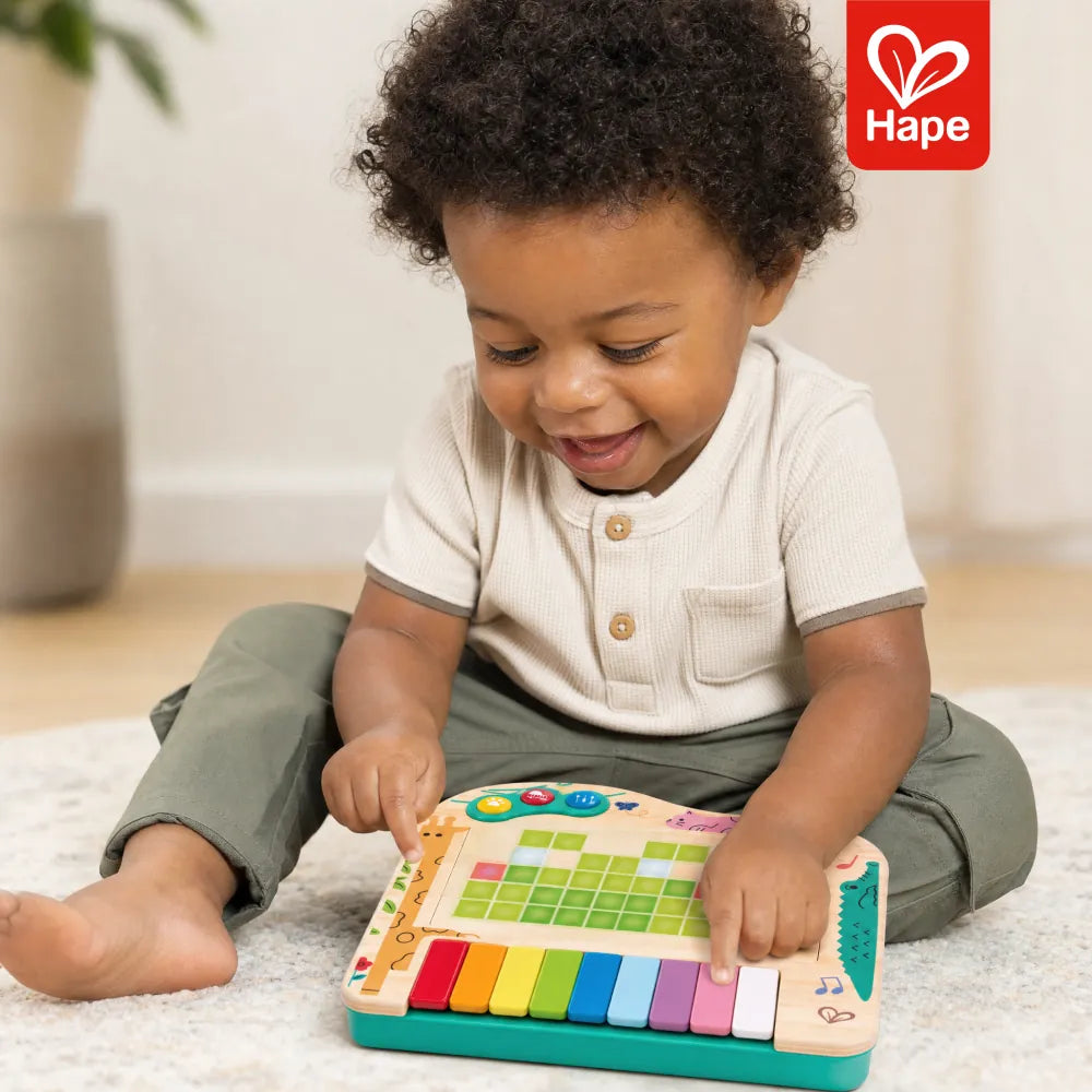 Bebê sorrindo e tocando o piano de pixels Hape no tapete